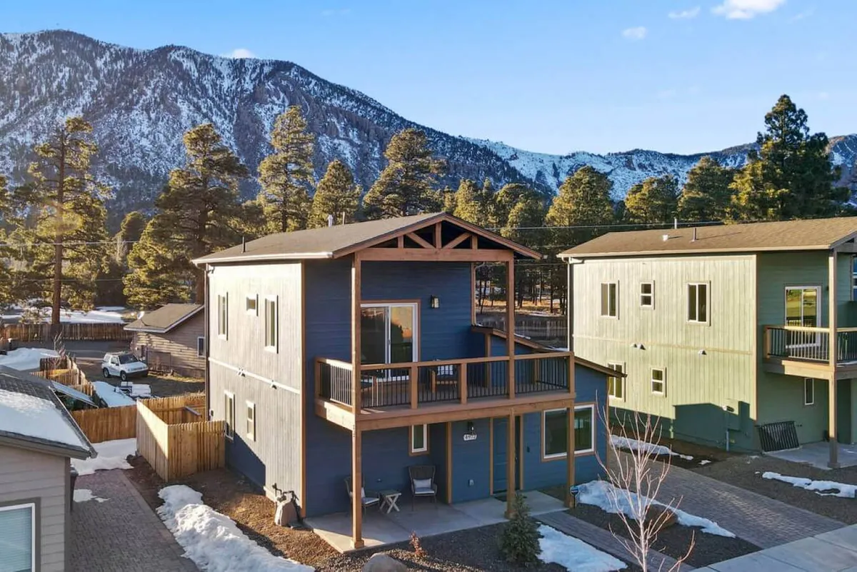 A colorful home with a wooden balcony is set against a dramatic mountain backdrop. The image emphasizes both the inviting exterior space and the proximity to awe-inspiring natural features, suggesting easy access to hiking and exploration. The sunset lighting adds warmth and highlights the appeal of evenings spent outdoors.