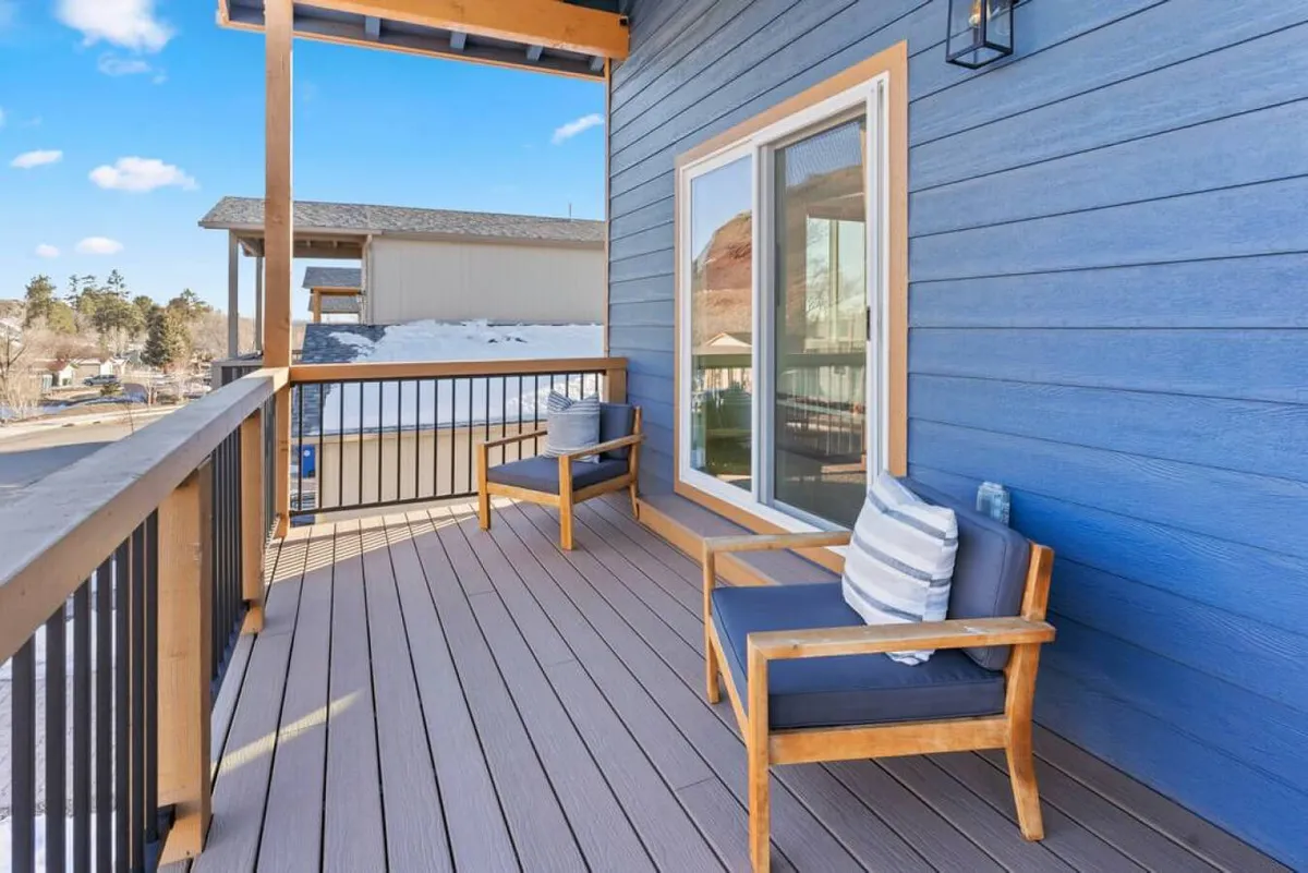 A serene wooden deck with comfortable outdoor seating is featured, framed by the blue house exterior. The setup invites gatherings or tranquil moments, ideal for watching sunsets or enjoying time with family and friends.