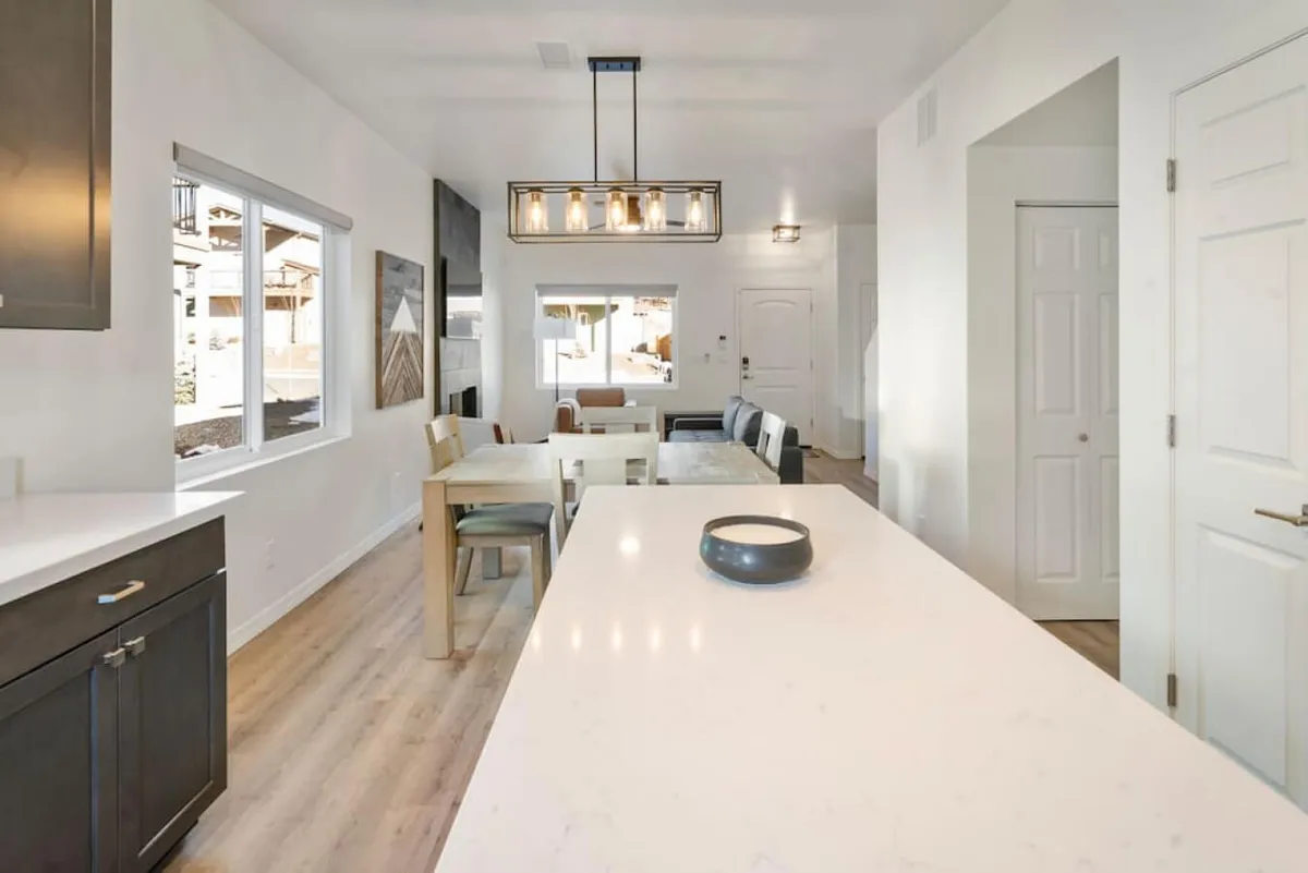 A spacious, modern open-plan area combining the kitchen, dining, and living zones. The kitchen island and dining table are arranged for gatherings or quiet moments, with ample light and a welcoming atmosphere, ideal for both productivity and leisure.