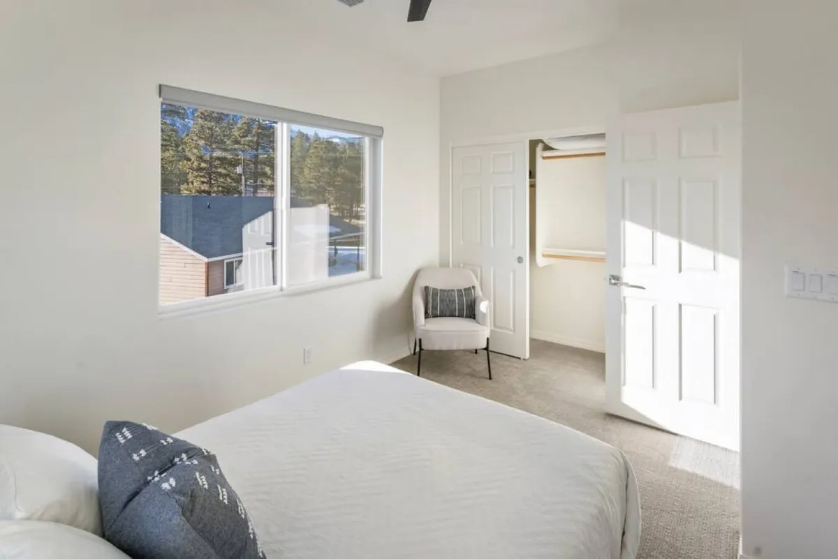 A tranquil bedroom featuring a plush bed, large window letting in soft natural light, a cozy reading chair, and a spacious closet. The atmosphere is quiet and restful, offering a sense of privacy and retreat.