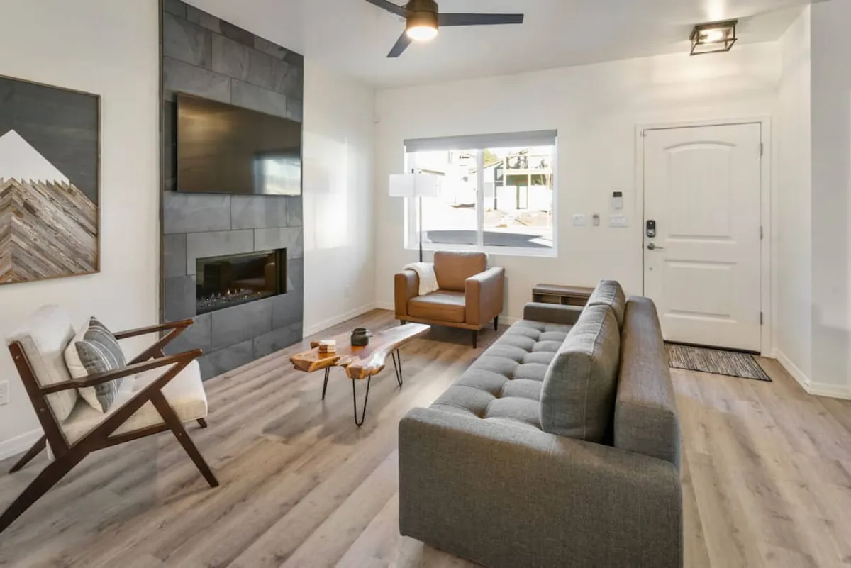 This image depicts a stylish living room featuring a modern sofa, a wooden coffee table, a contemporary fireplace, and large windows that flood the space with natural light. Artwork adds an extra touch of sophistication while the inviting seating area suggests a perfect spot for socializing or relaxing after a day outdoors.