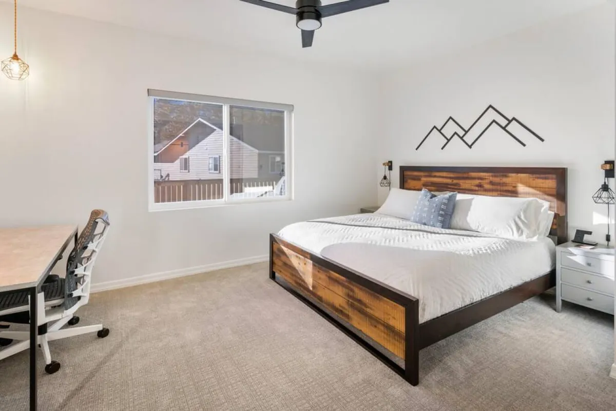 A cozy bedroom with a bed, desk, mountain-inspired decor, and a large window that floods the space with natural light. The room feels welcoming and balanced for both relaxation and quiet morning routines.