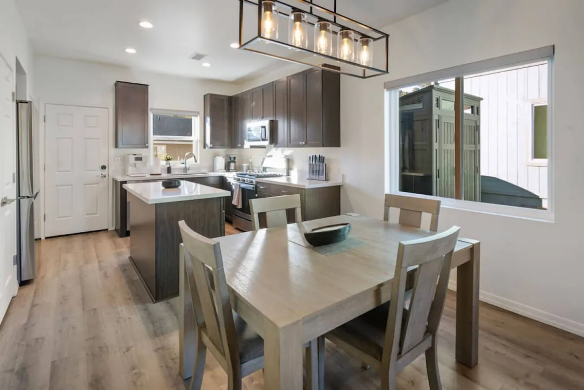 A warm and welcoming view of the dining area and kitchen, featuring a modern dining table, kitchen island, and contemporary lighting. The setup is ideal for family meals, celebrations, or casual gatherings, with an inviting ambiance that encourages connection.