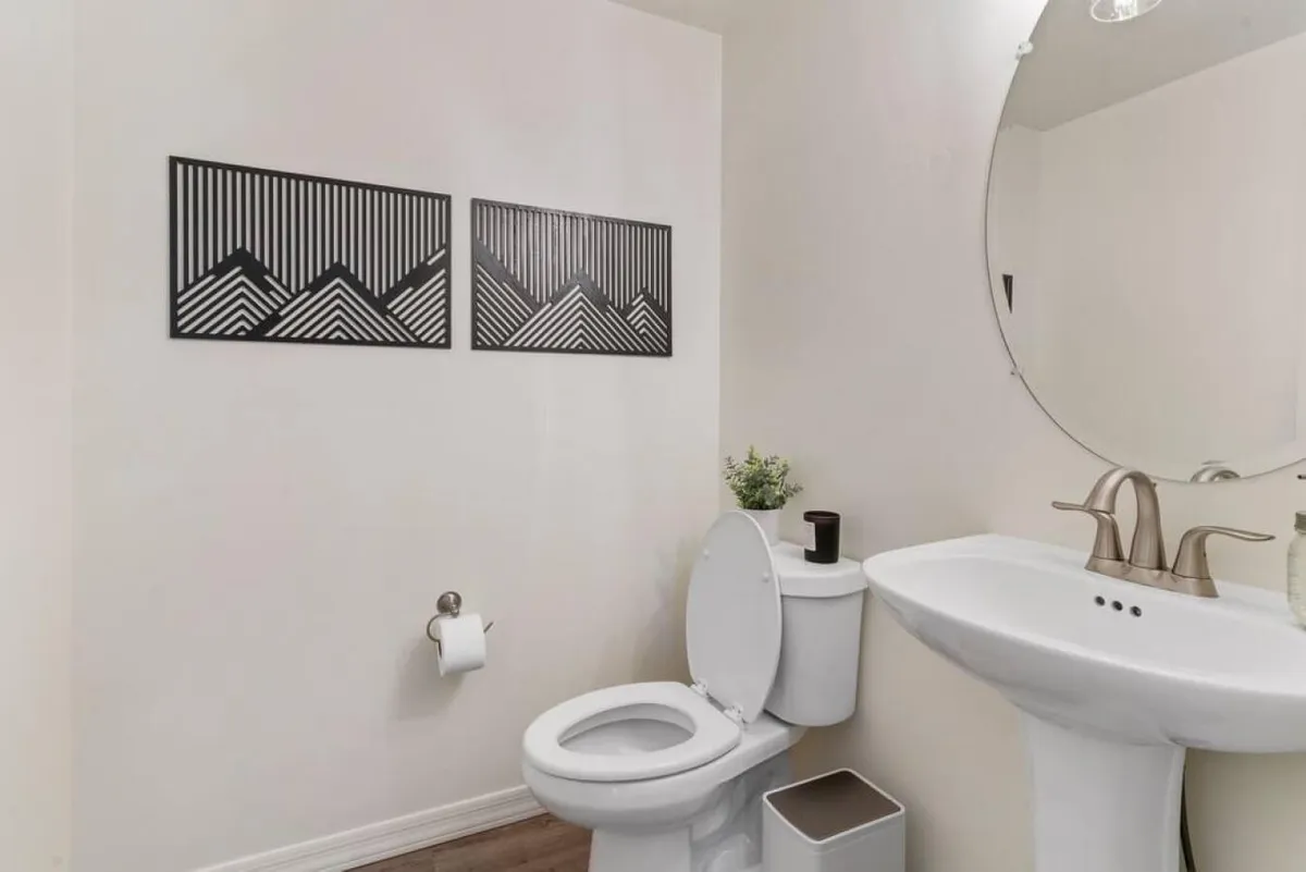 A minimalist powder room with a sleek sink, toilet, mirror, and tasteful wall art. The uncluttered design emphasizes serenity and practicality, ideal for guests or quick refreshes.