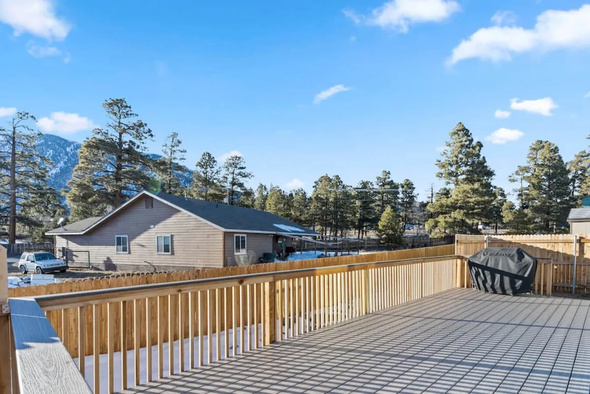 A spacious wooden deck looks out over a landscape of tall trees and distant mountains, providing a tranquil spot for outdoor dining or relaxing after a day on the trails. The deck’s vantage point frames panoramic mountain views, inviting guests to unwind while soaking in the natural beauty surrounding the home.